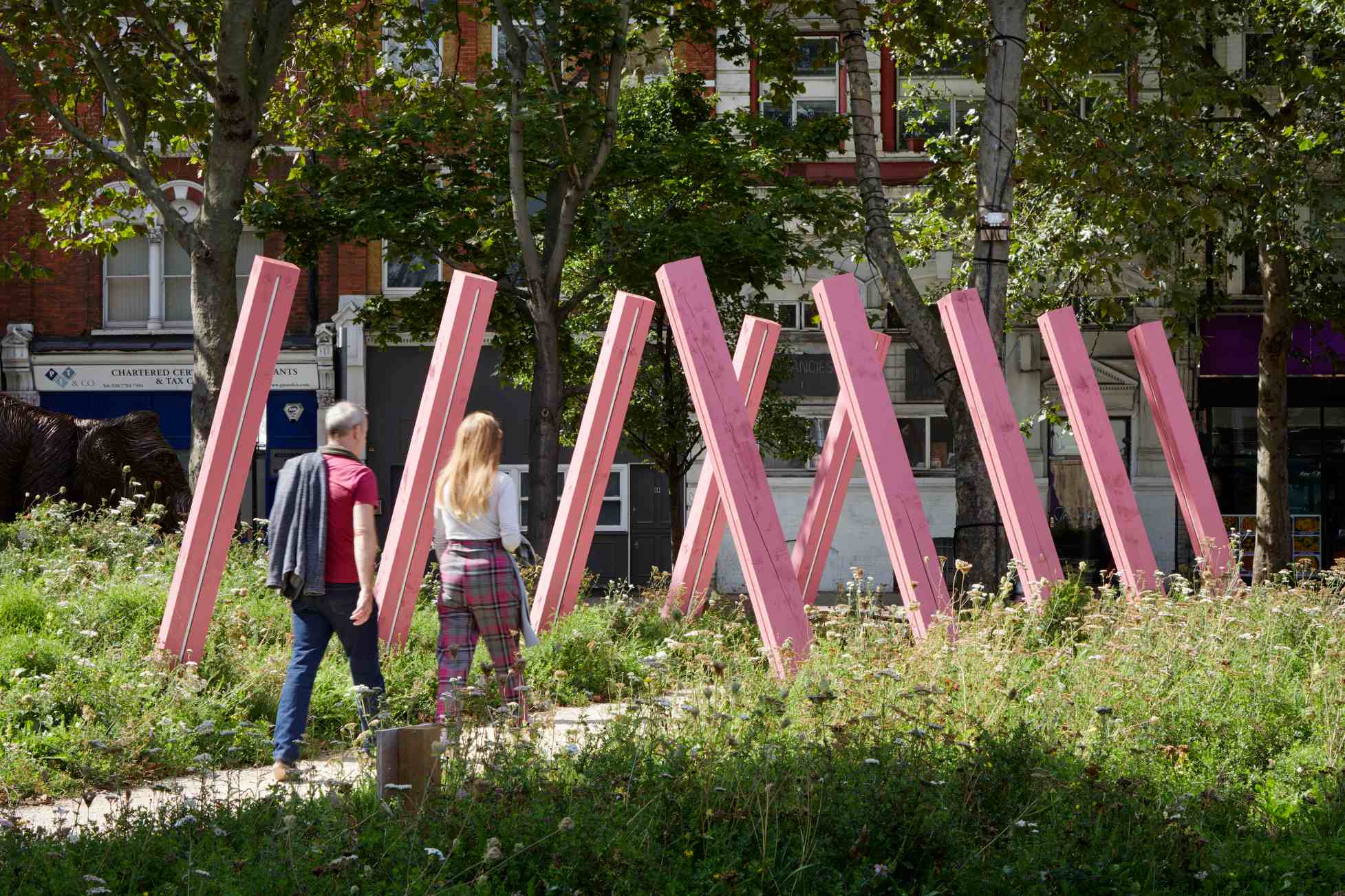 The Meadow at Elephant Park, showing two people walking underneath the  pink diagonal structures which create a triangle above the path