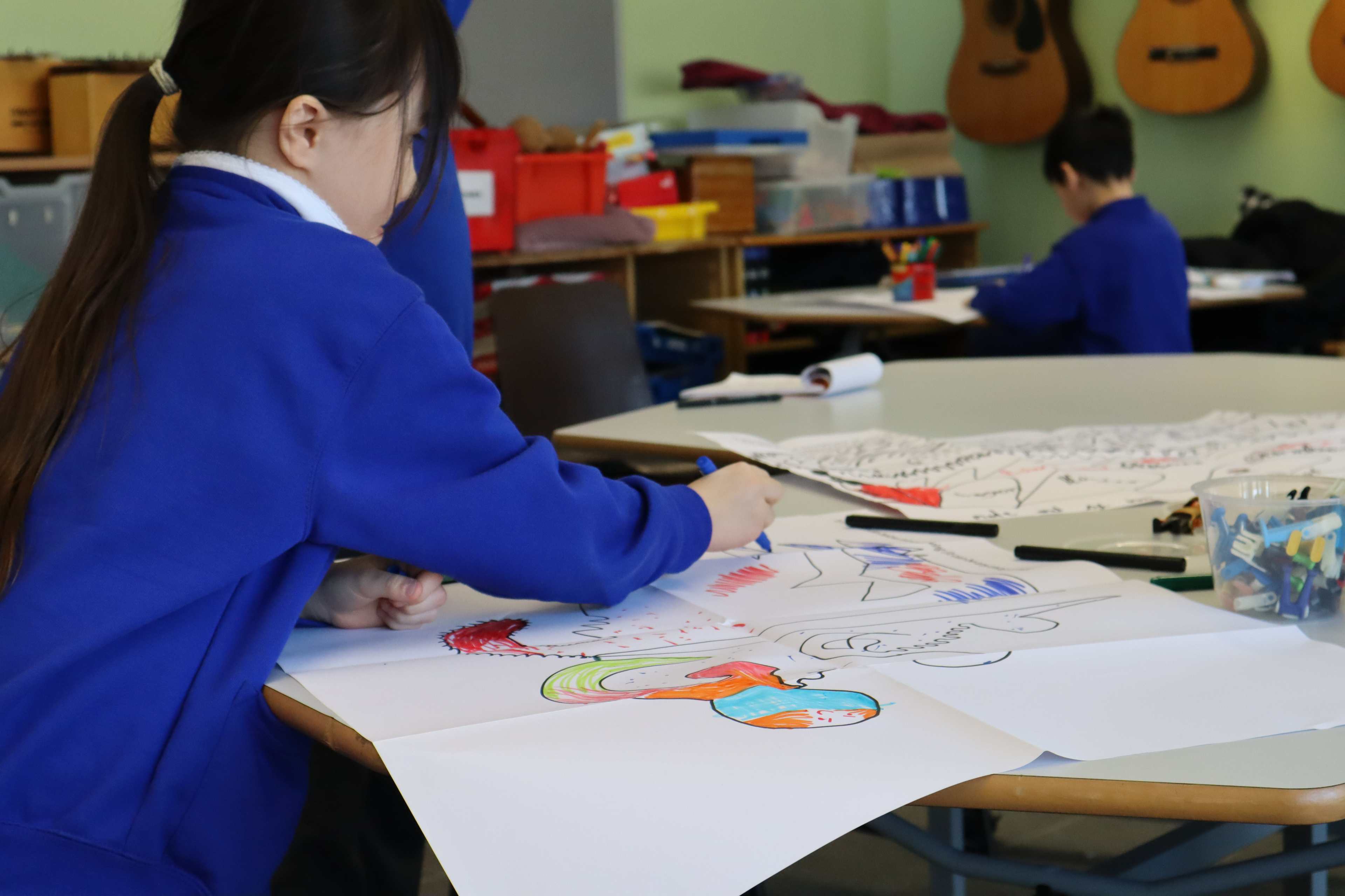 A child wearing a blue sweatshirt sitting at a table colouring in a picture.