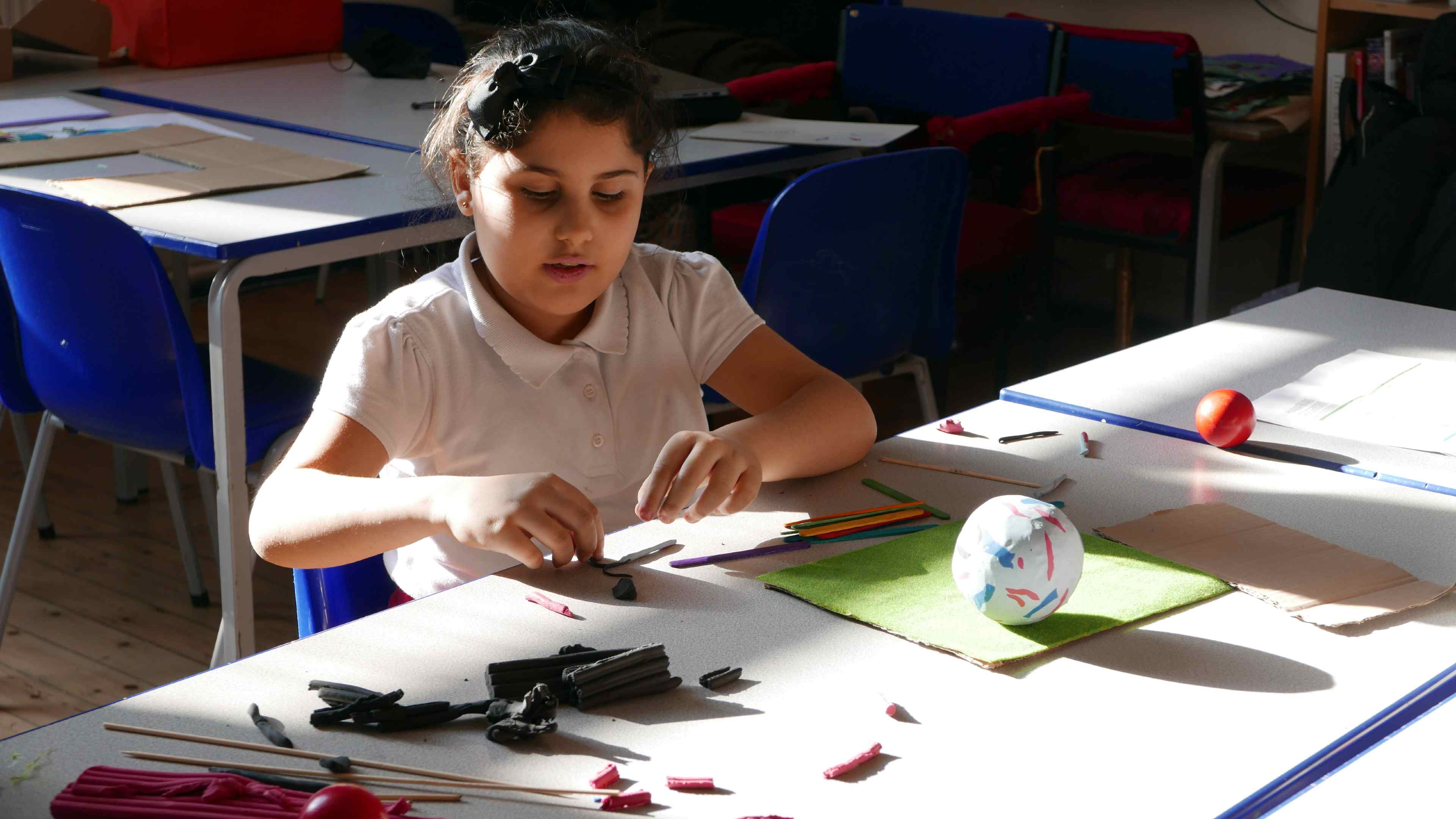 A girl wearing a white polo shirt playing with clay sitting at a table.