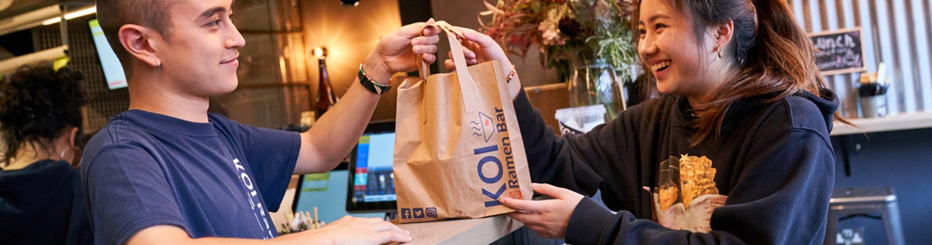 A man handing a paper Koi Ramen bag to a customer