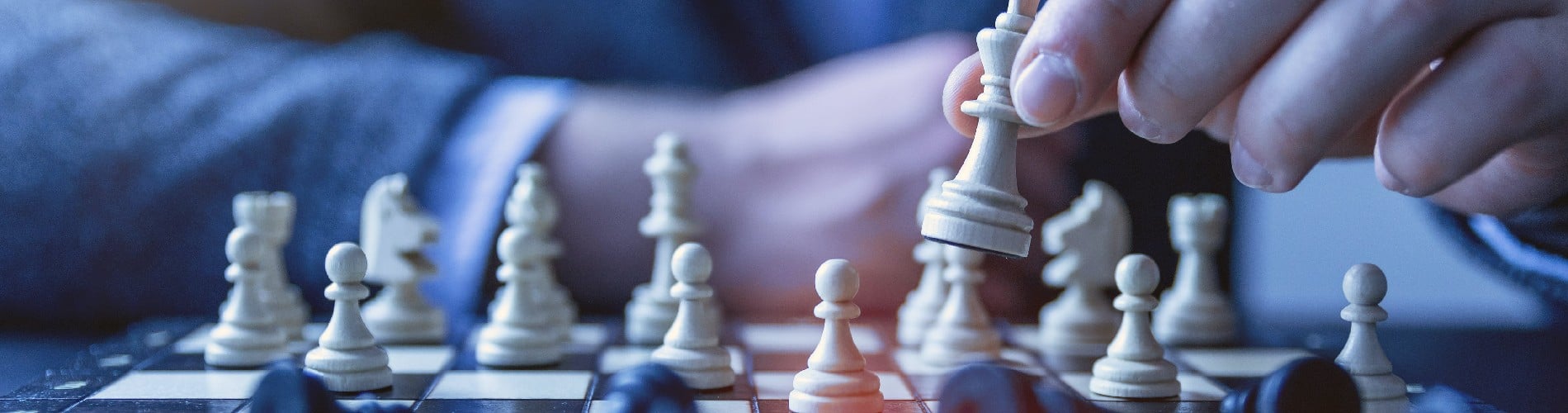 Close up of a man's hand holding a chess piece during a game of chess with the other pieces scattered on the board